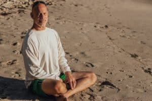 A photo of a man seated on beach sand demonstrates the joy of knowing that you are aging without a shrinking penis.