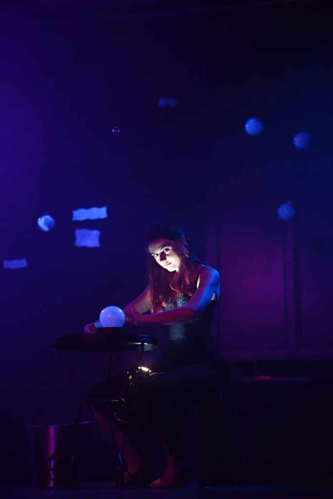 A female healer poised on a stool surrounded by magical items casting spells for penis growth with an air of determined concentration