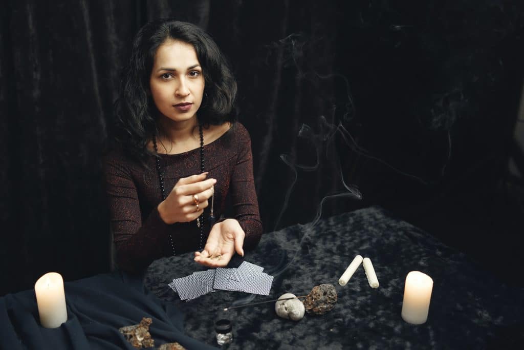 A mystical female healer surrounded by glowing candles and ancient tarot cards preparing to cast potent spells for penis growth